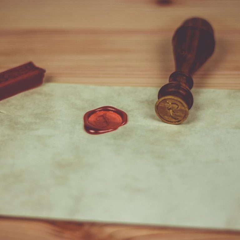 A pool of red sealing wax poured on an envelope next to a brass stamp