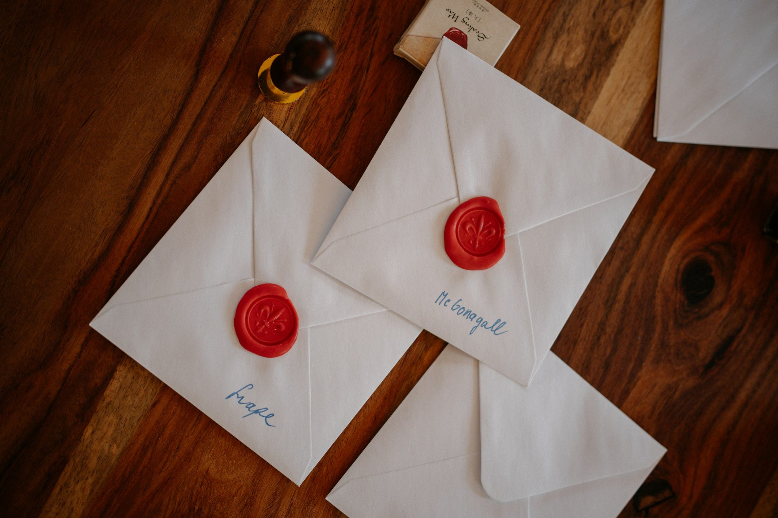 Three white envelopes closed with red wax seals on a wooden table